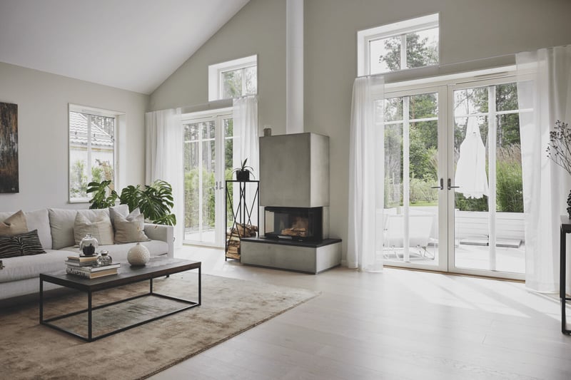 Ljust skandinaviskt vardagsrum med stora vitmålade fönster och altandörrar mot trädgården.